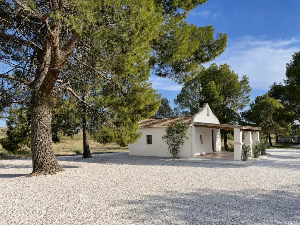 Renovated wedding chapel at Finca Moñino with white gravel courtyard and Mediterranean pine trees in Abanilla, Spain.